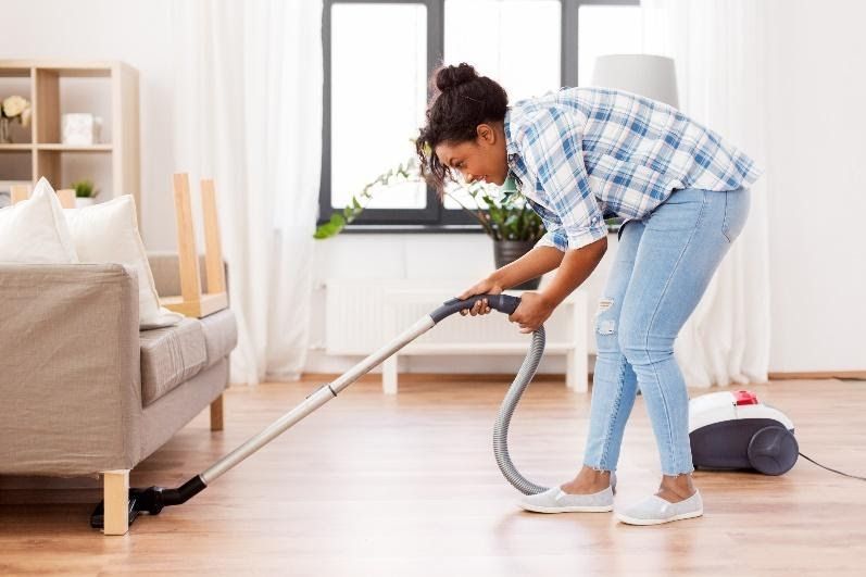 a lady using a vacuum cleaner to remove dust from under her chairs.