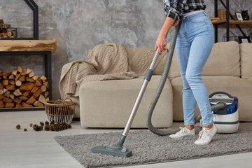 Cropped image of beautiful young woman using a vacuum cleaner while cleaning carpet in the house
